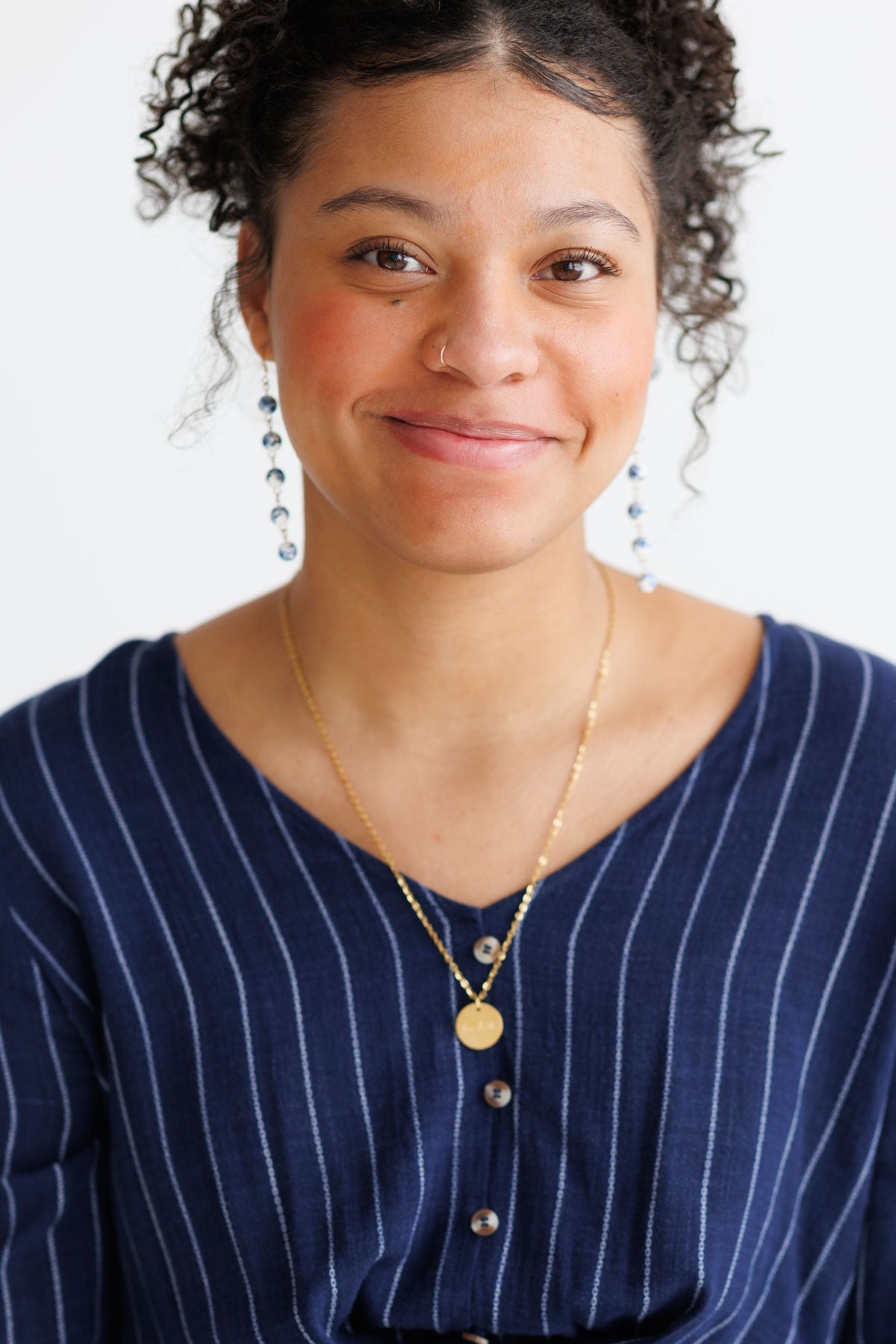 Woman wearing blue-and-white porcelain drop earrings with round charms and gold-tone hooks