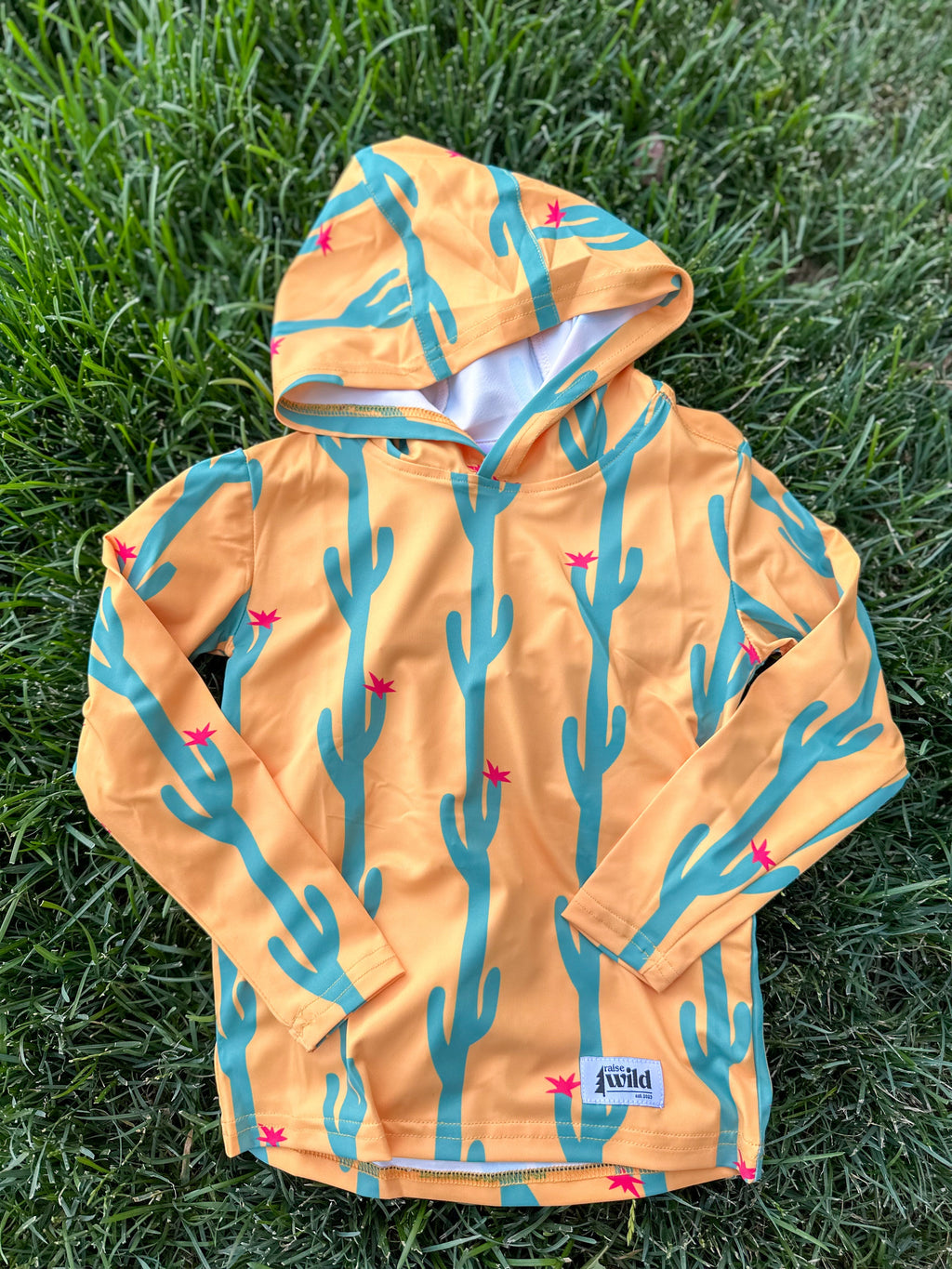 Kids UPF 50 sun hoodie in light orange with cactus and flower prints, front pocket