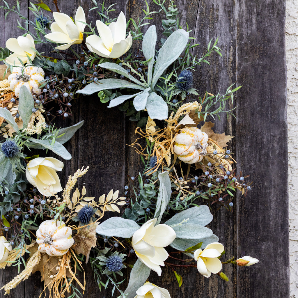 Sage wreath close view of white magnolia-style flowers, blue thistle, and berry stems