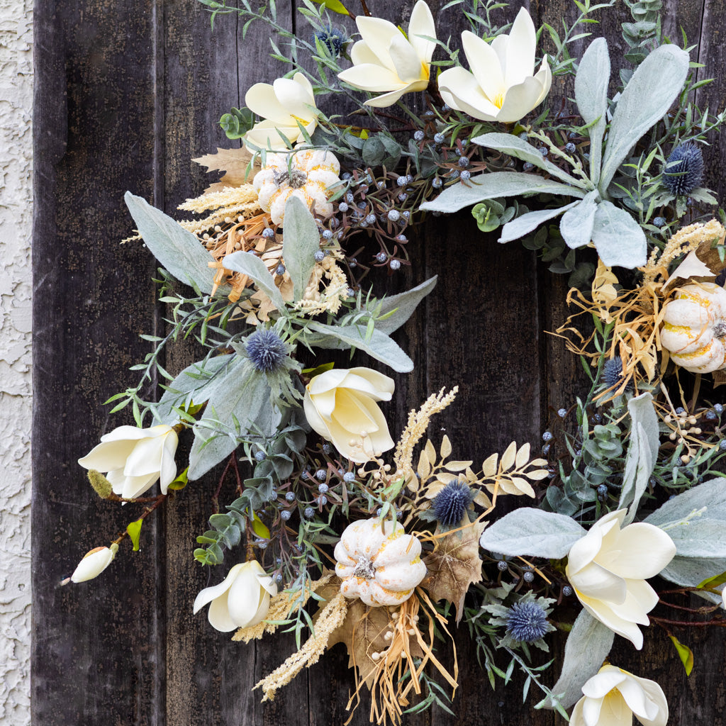 Sage wreath with layered white petals, eucalyptus foliage, blue thistle, and dried grass strands