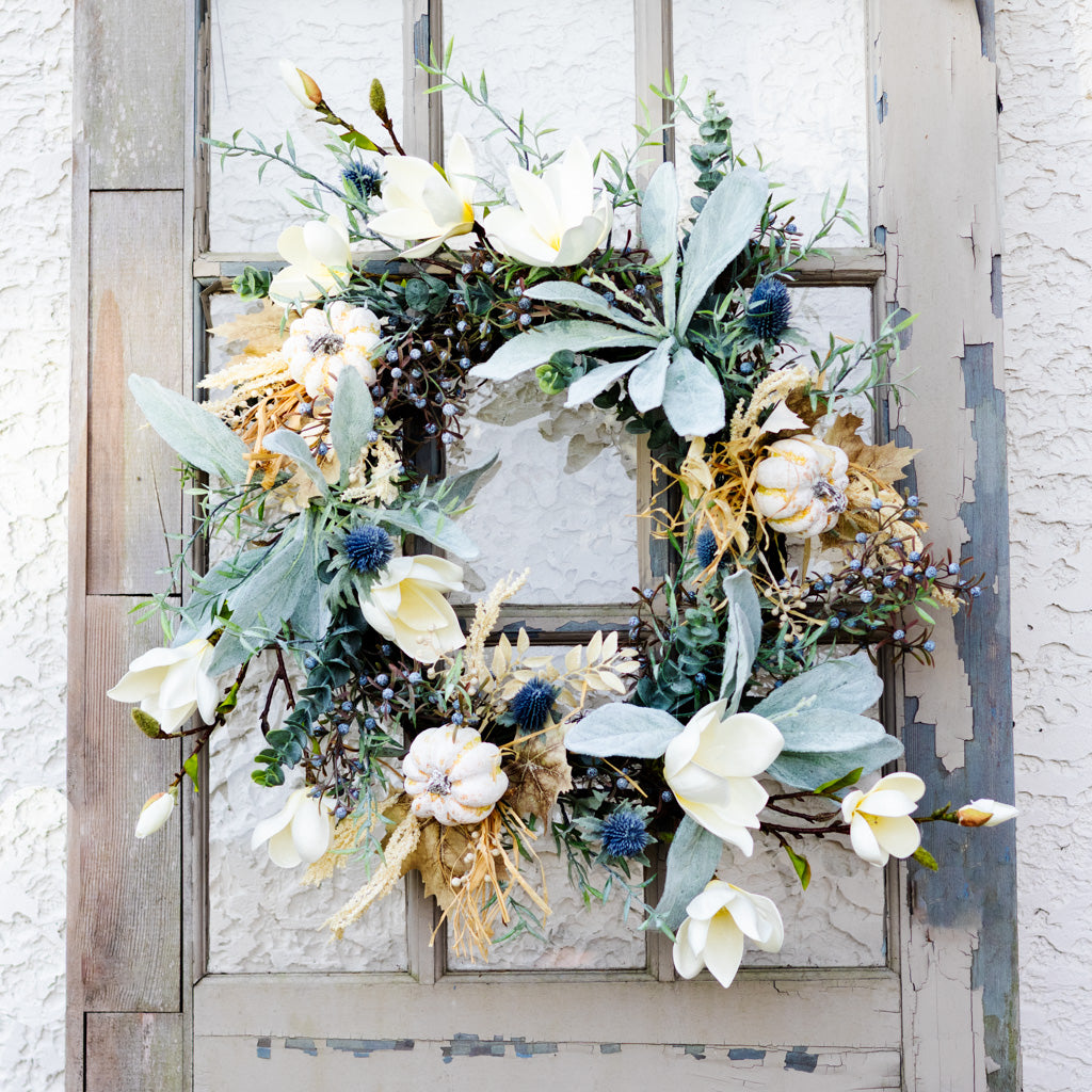 Sage wreath featuring white flowers, gray-green leaves, blue thistle clusters, and pinecone-like buds