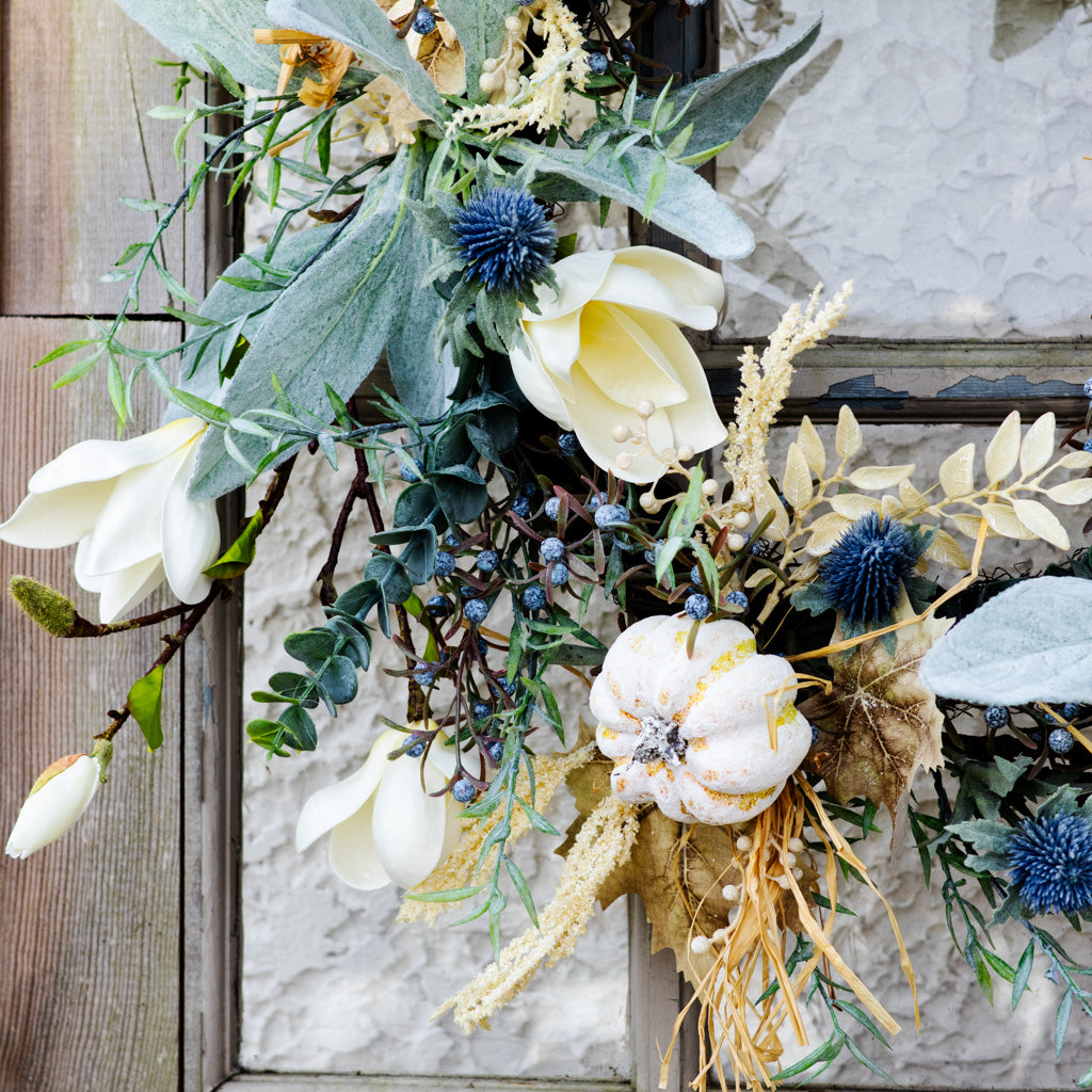 Sage wreath on rustic frame with white petals, blue thistle florets, and hanging dried stems