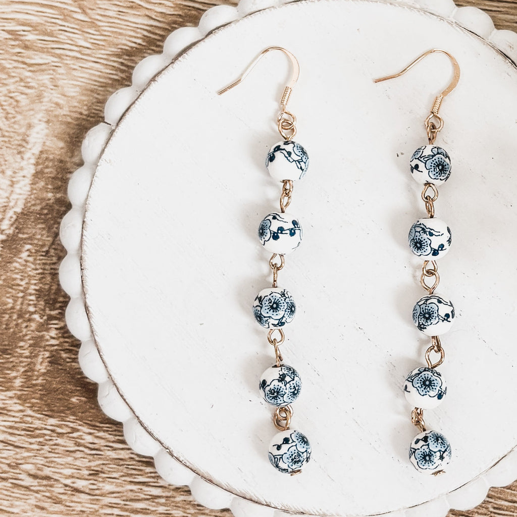 Pair of blue porcelain bead drop earrings on white display card; gold-tone hooks