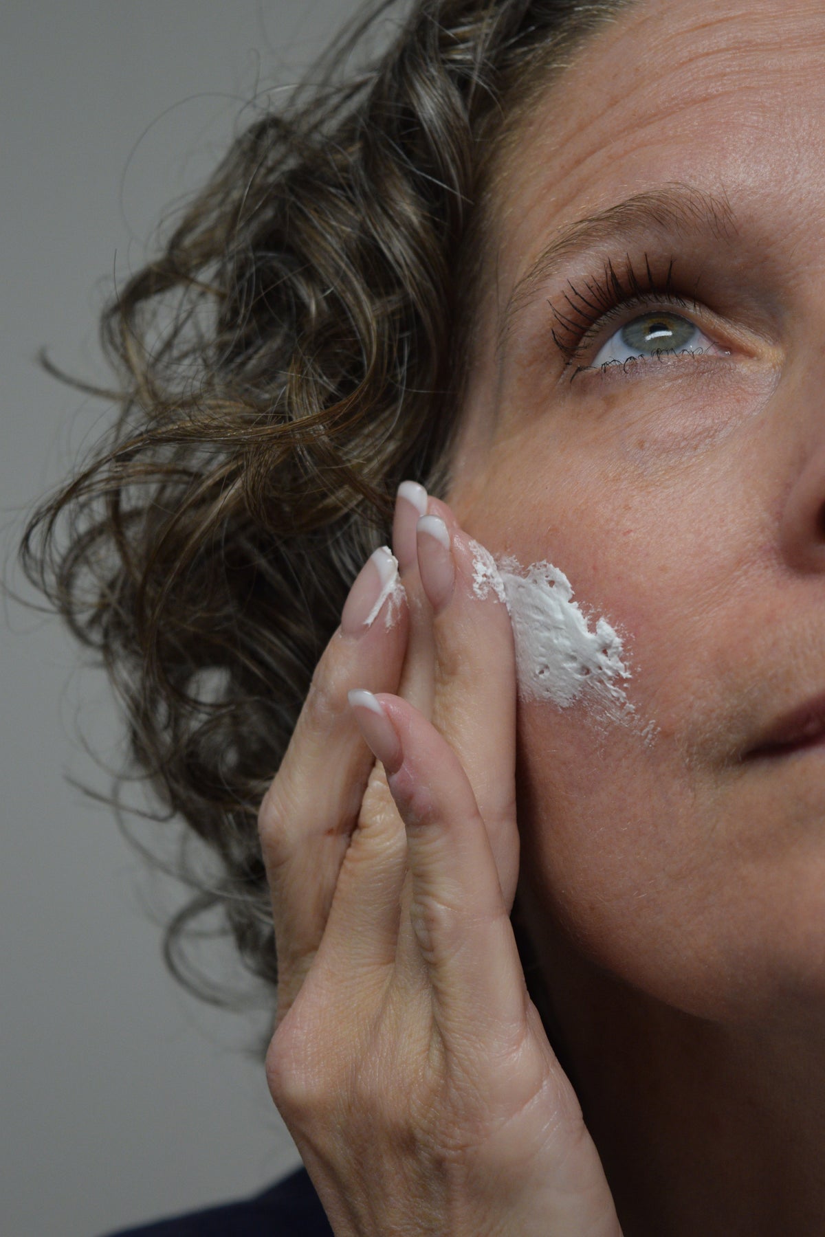 Woman applying white whipped lotion to cheek near eye