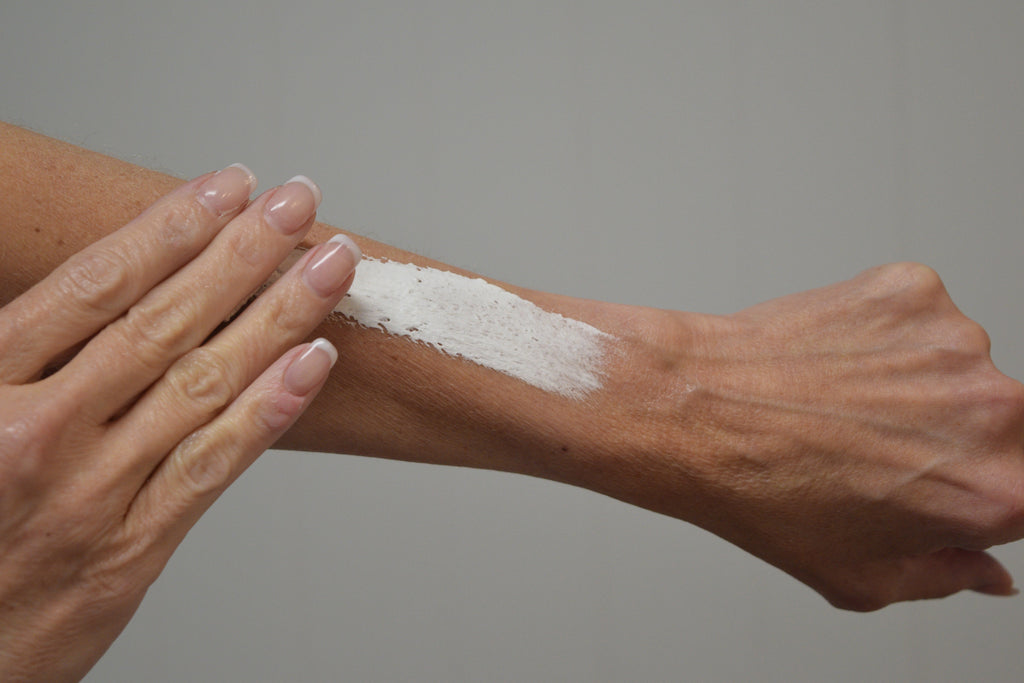 Hands smoothing white whipped lotion across forearm
