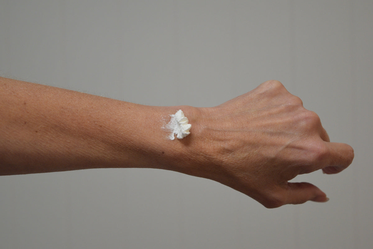 Person spreading white whipped lotion on forearm skin