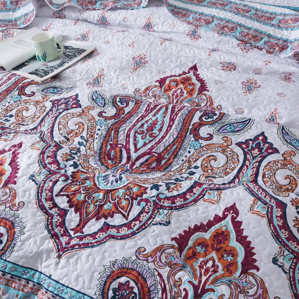 Close-up of white quilt with large paisley medallion in blue, burgundy, and orange tones