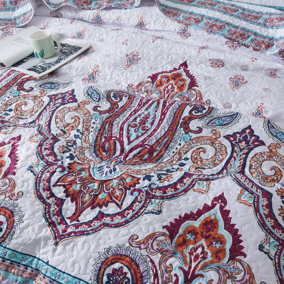 Close-up of white quilt with large paisley medallion in blue, burgundy, and orange tones