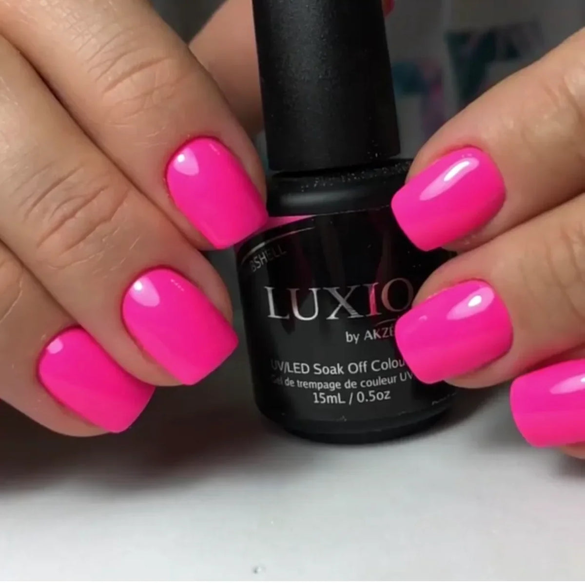 Luxio gel polish bottle with bright fuchsia manicured nails, glossy