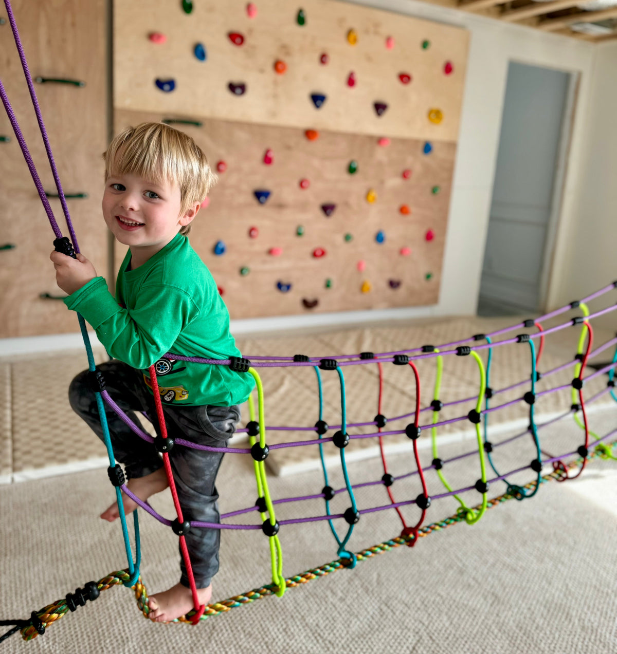 Multicolor rope suspension bridge indoors with child sitting on net