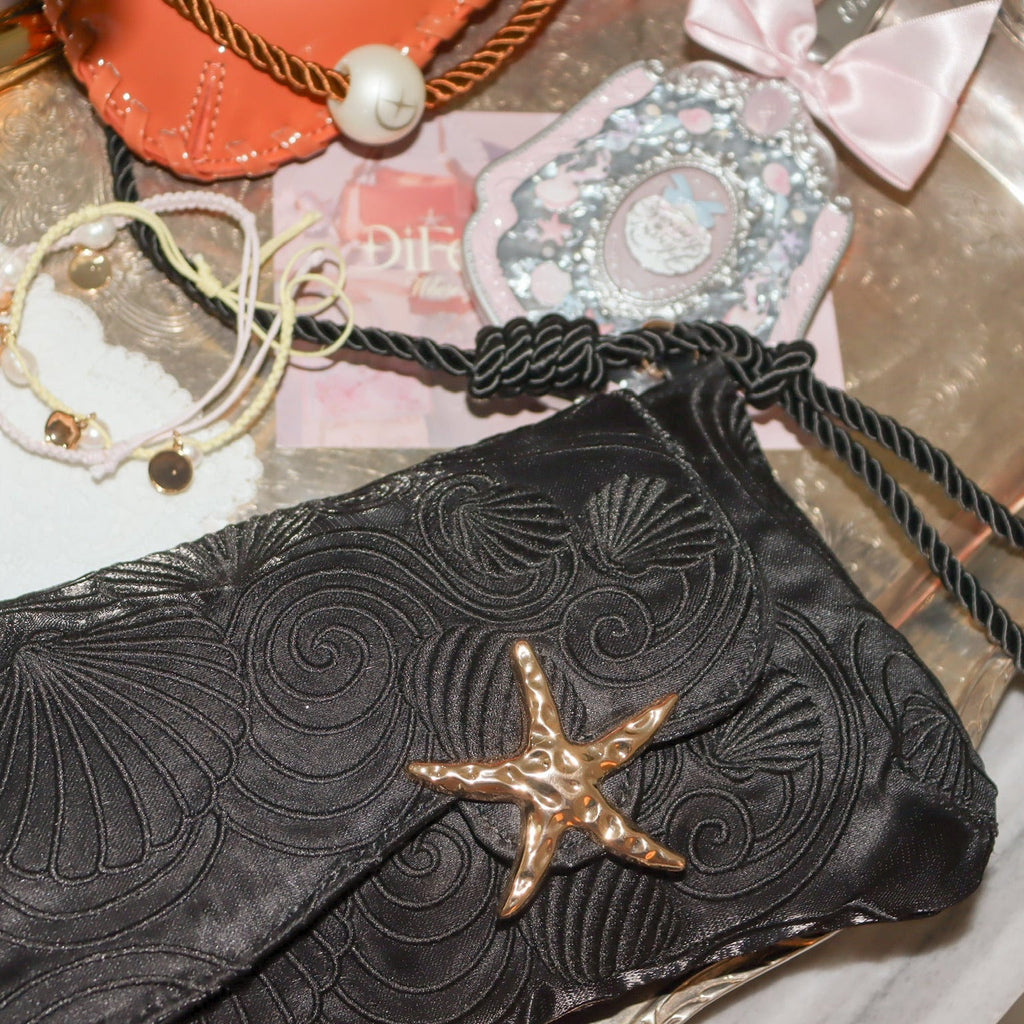 Starfish clasp on a black embroidered shoulder bag with textured swirling pattern