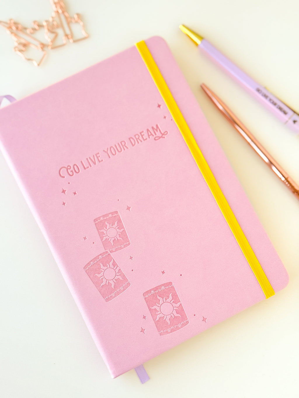 Pink dream notebook with embossed sun icons, yellow elastic strap and lavender ribbon