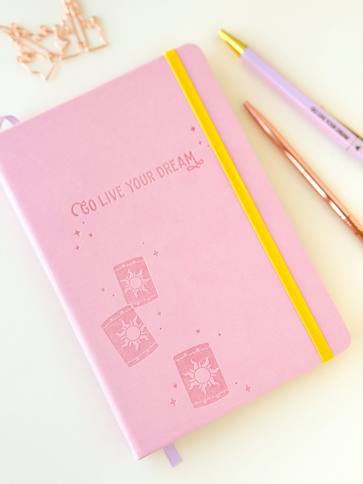 Pink dream notebook with embossed sun icons, yellow elastic strap and lavender ribbon