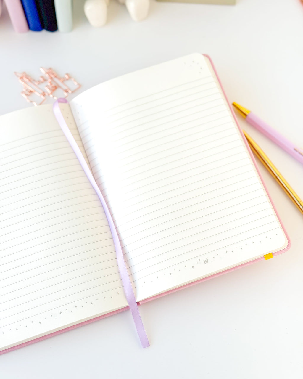 Open pink notebook with lined pages and purple spine ribbon, yellow edge