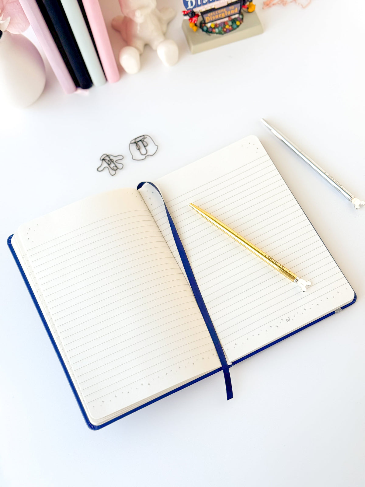 Open blue notebook with ruled pages, dark-blue cover, and gold pens