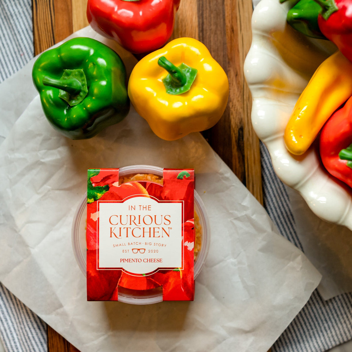 Pimento cheese spread tub on paper with green, yellow, and red bell peppers nearby
