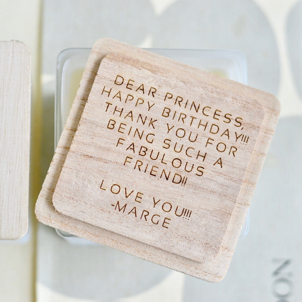 Wooden candle lid with engraved greeting and name text, light tan square shape