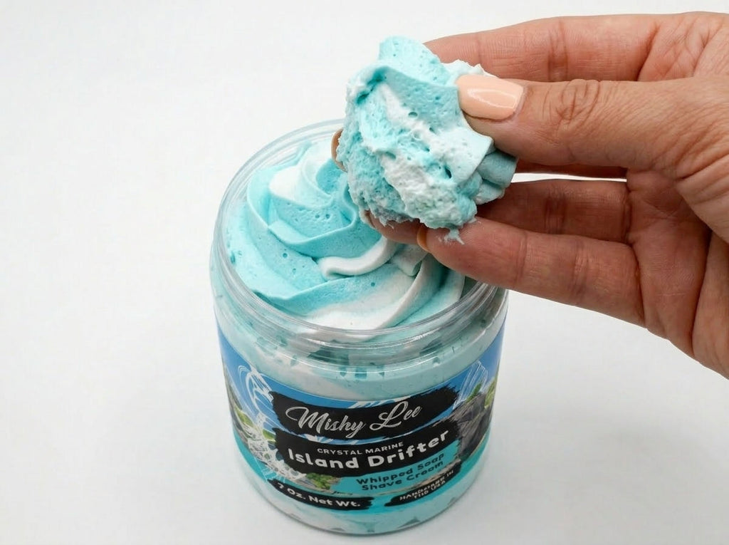 Hand holding a scoop of turquoise whipped soap and shave cream from the jar