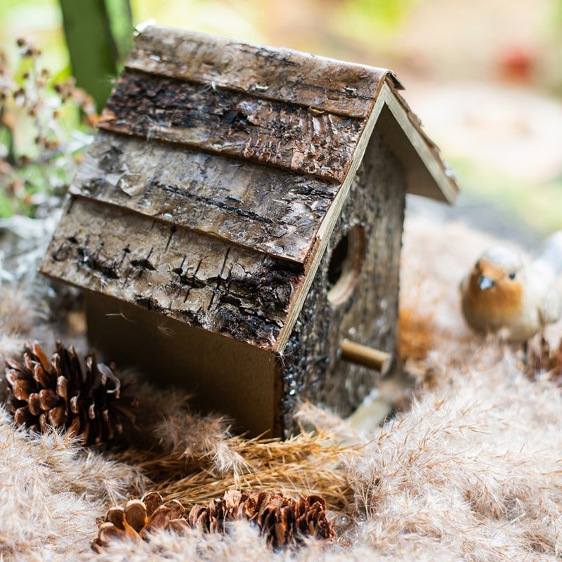 Weathered wood bird house with round opening, side mounting bar, and layered shingle roof