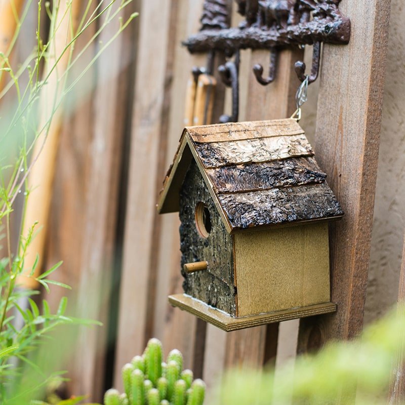Hanging weathered wood bird house with round entrance opening and small side perch