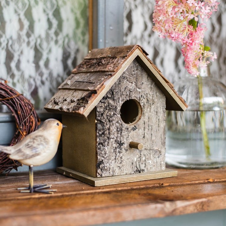 Weathered wood bird house with circular entrance hole, front perch, and roof shingles
