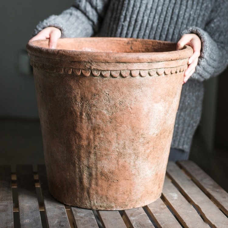 Large terracotta red concrete planter pot, weathered finish, scalloped rim.