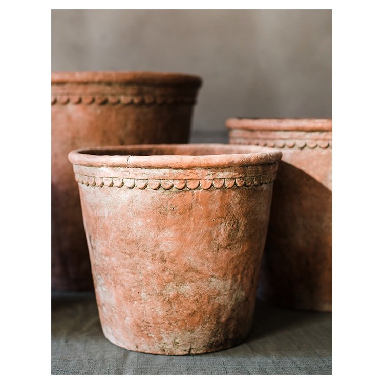 Terracotta red concrete planter pot close-up, scalloped rim and speckled texture