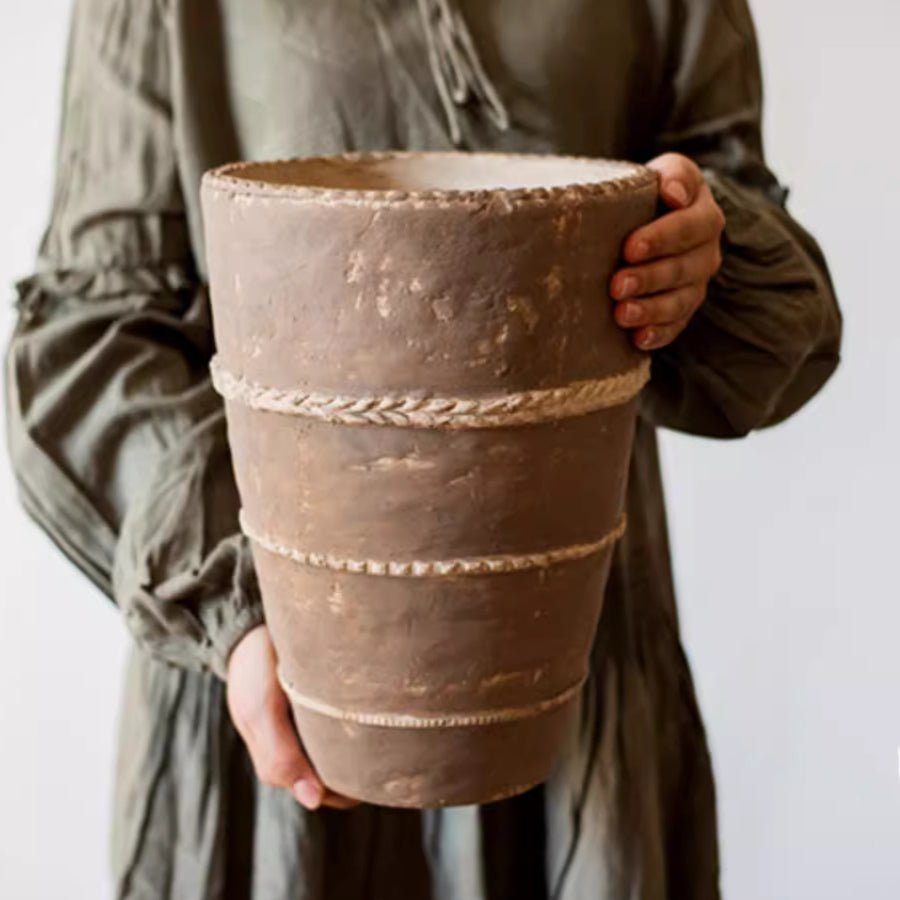 Terracotta-toned planter with braided rope bands held in hands, front view