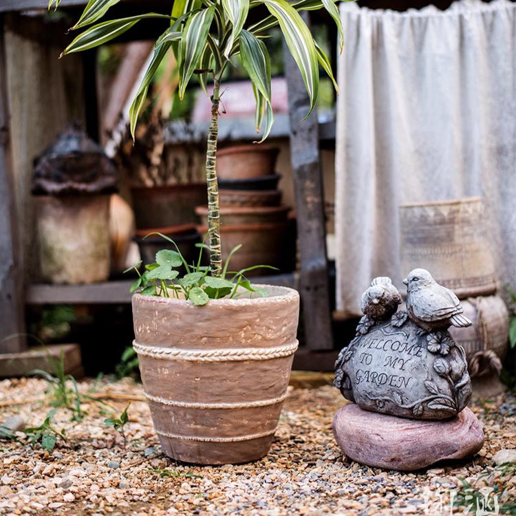 Terracotta-toned planter with braided rope bands surrounded by gravel and plants