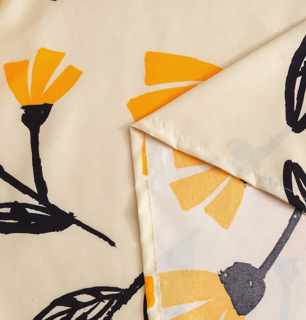 Ivory bedding fabric with yellow fleur floral print and black botanical stems, folded