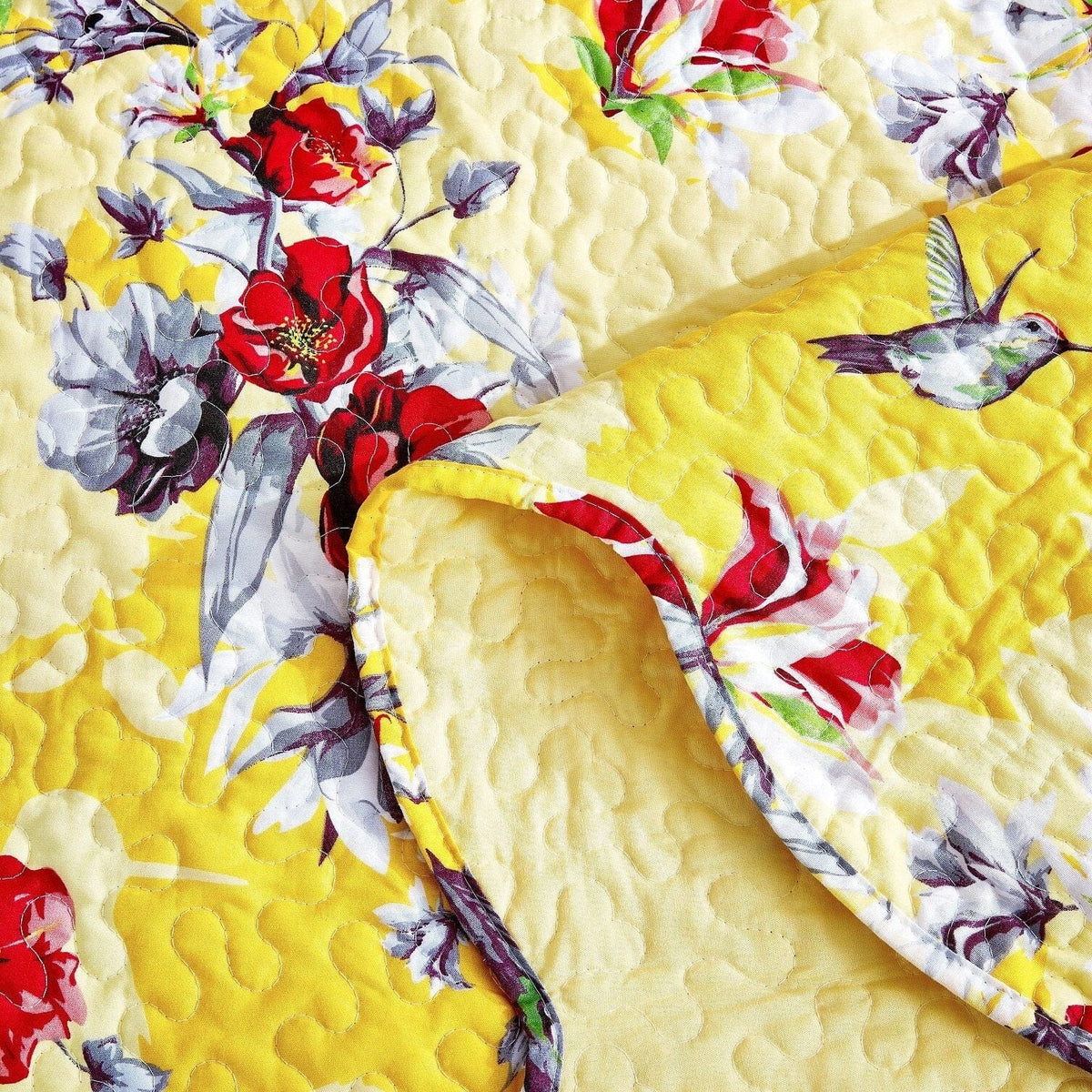 Quilted yellow bedspread detail with red, purple, and white floral and bird pattern