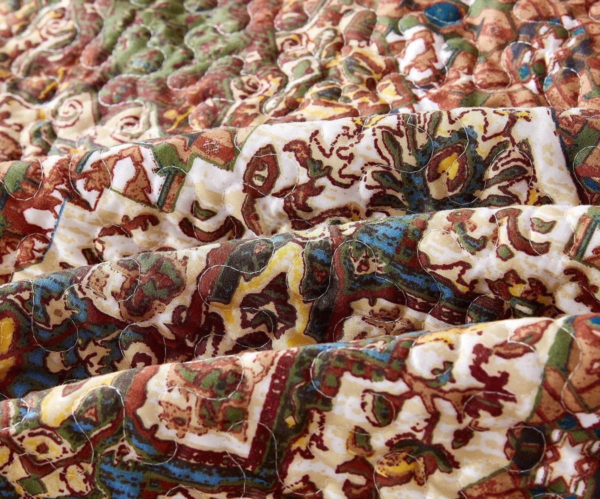 Close-up of quilted fabric with colorful folk medallion pattern in earthy reds and teals