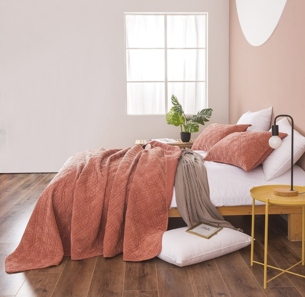 Terracotta coral velour corduroy bedspread draped over bed with two matching pillows