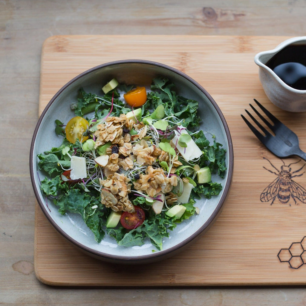 Kale salad bowl topped with granola, sprouts, and cherry tomatoes