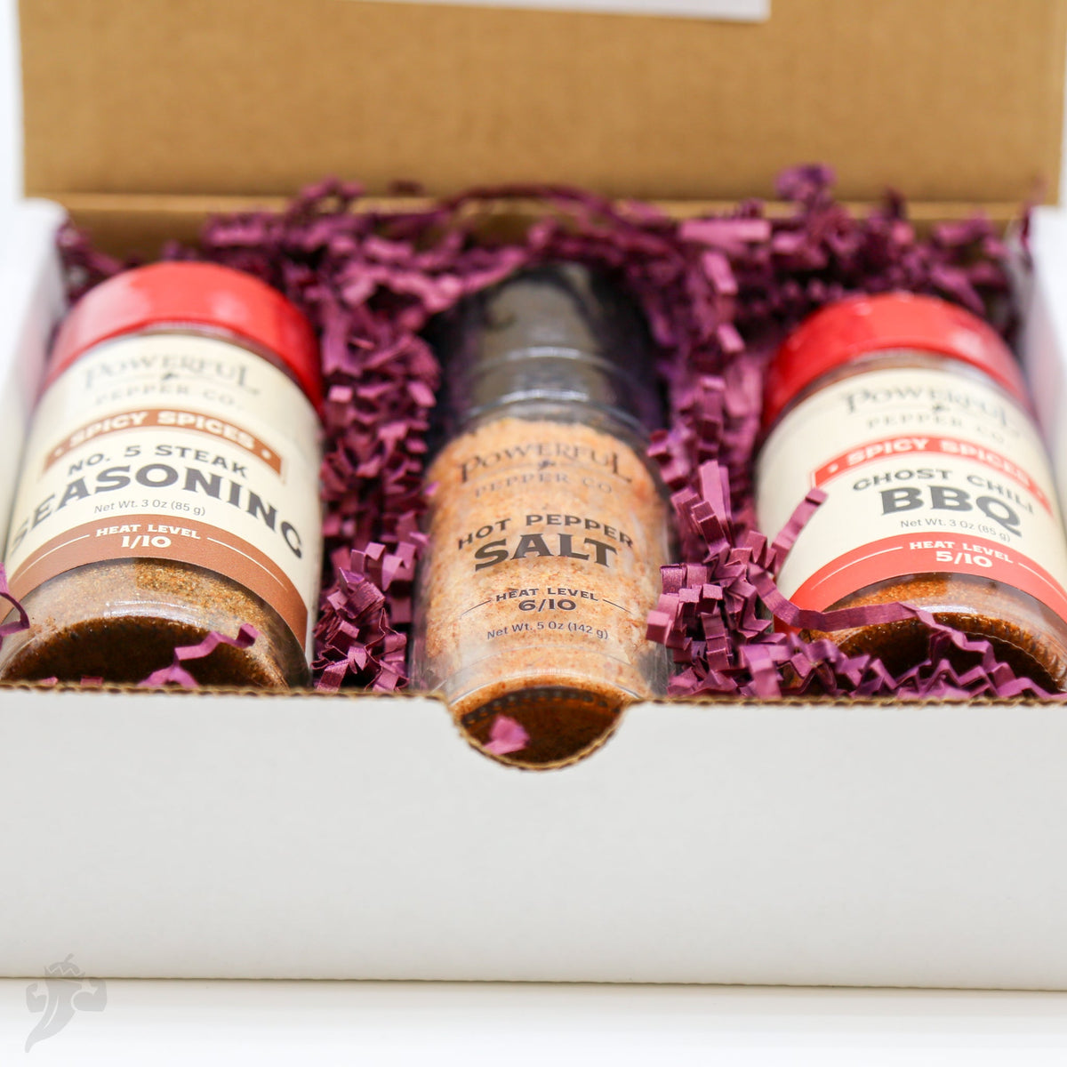 Close-up of three BBQ seasoning bottles in tray with purple shredded filler