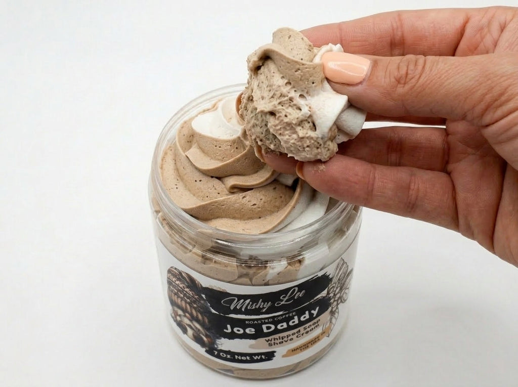 Hand holding a scoop of whipped soap from the jar, beige and frothy texture