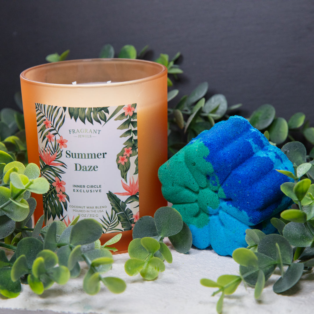 Orange glass candle next to blue and green flower-shaped bath bomb
