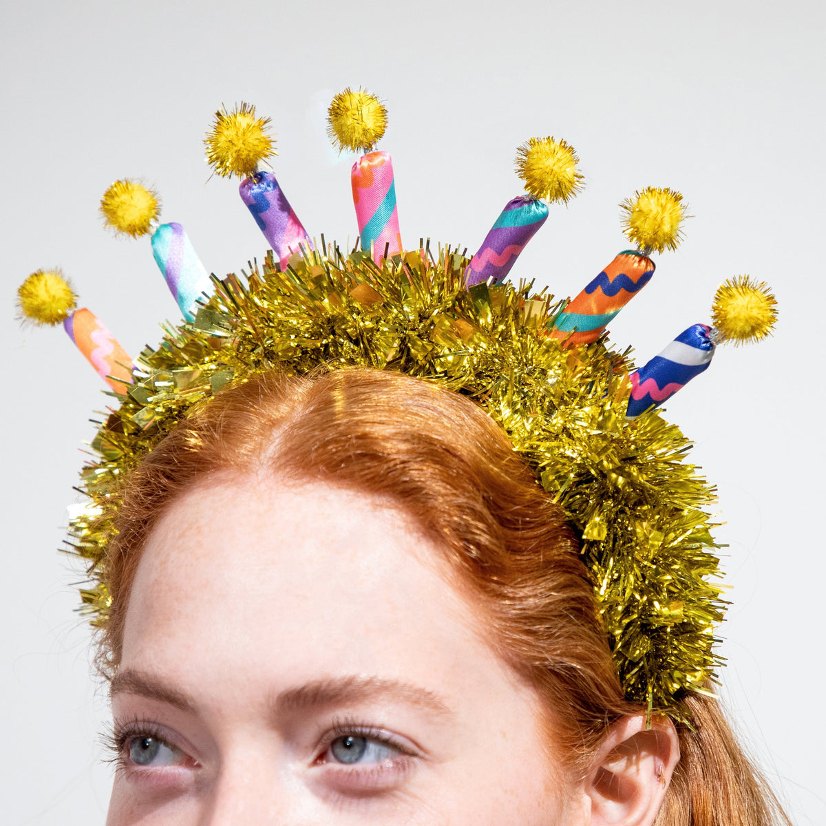Gold tinsel headband with rainbow candle cutouts and yellow pom-pom topper details