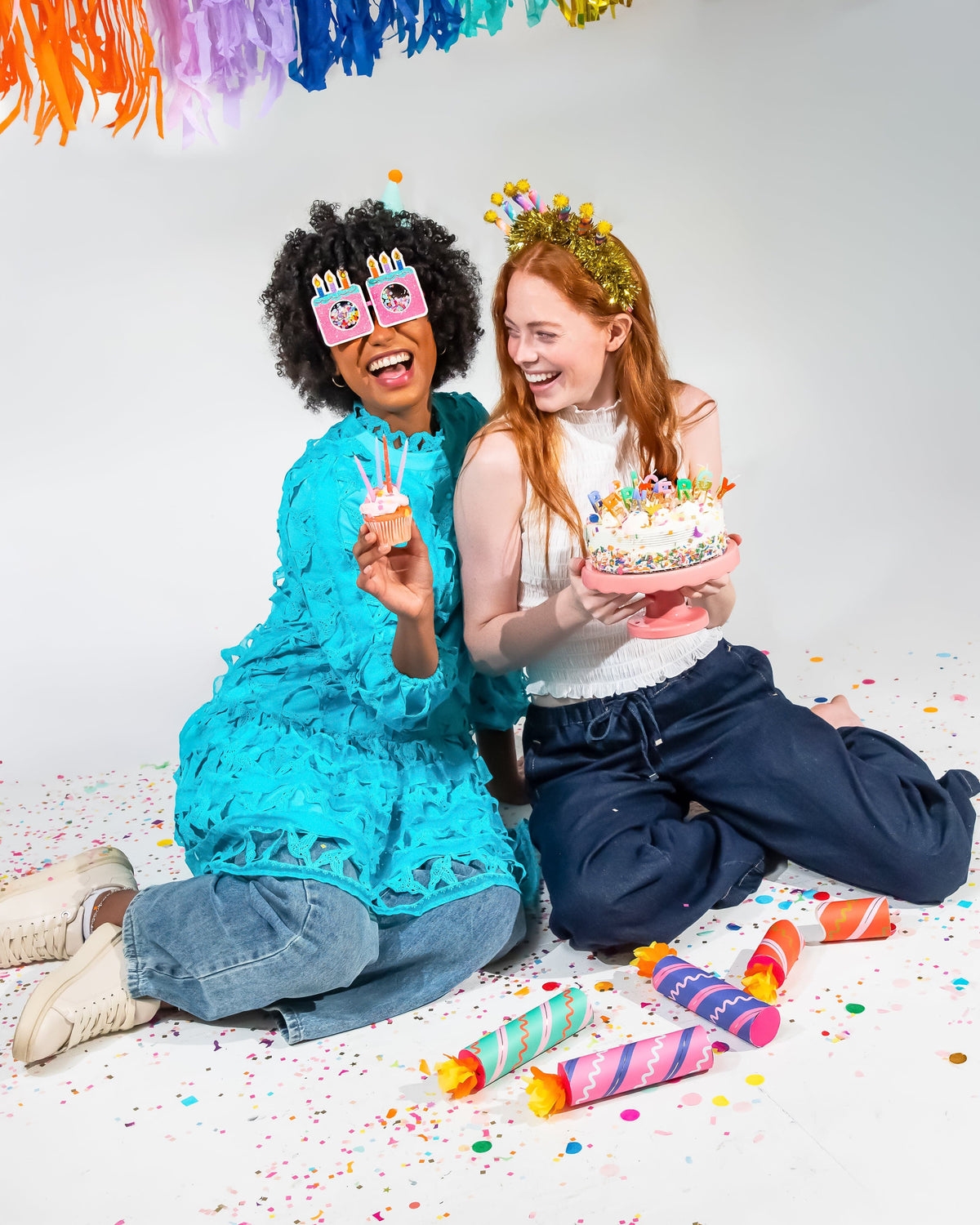 Birthday party cracker set with confetti, two people holding crackers beside a cake
