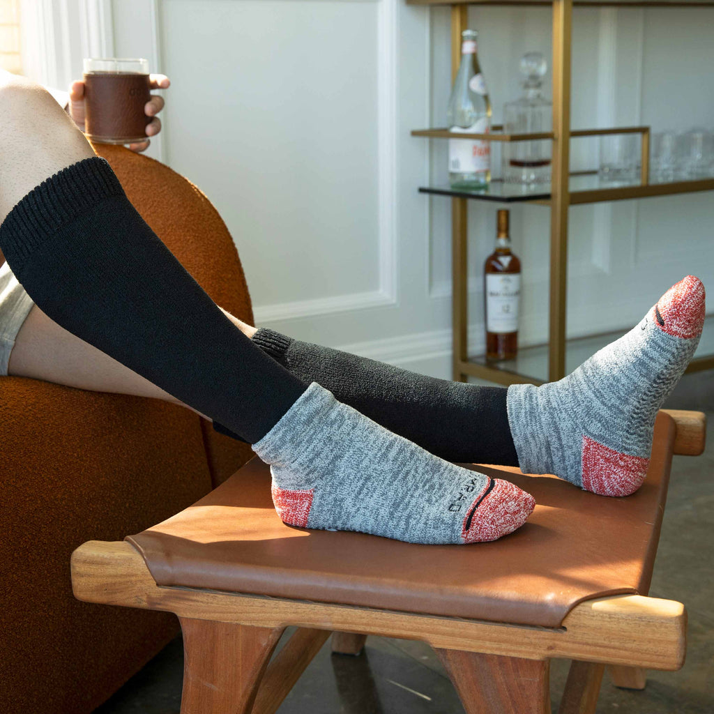 CozyGrip compression slipper socks on feet: black cuff, gray foot, red anti-slip grips