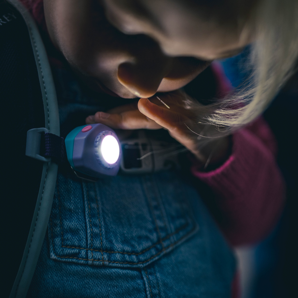 Kids headlamp worn on denim, glowing white LED light pointed forward