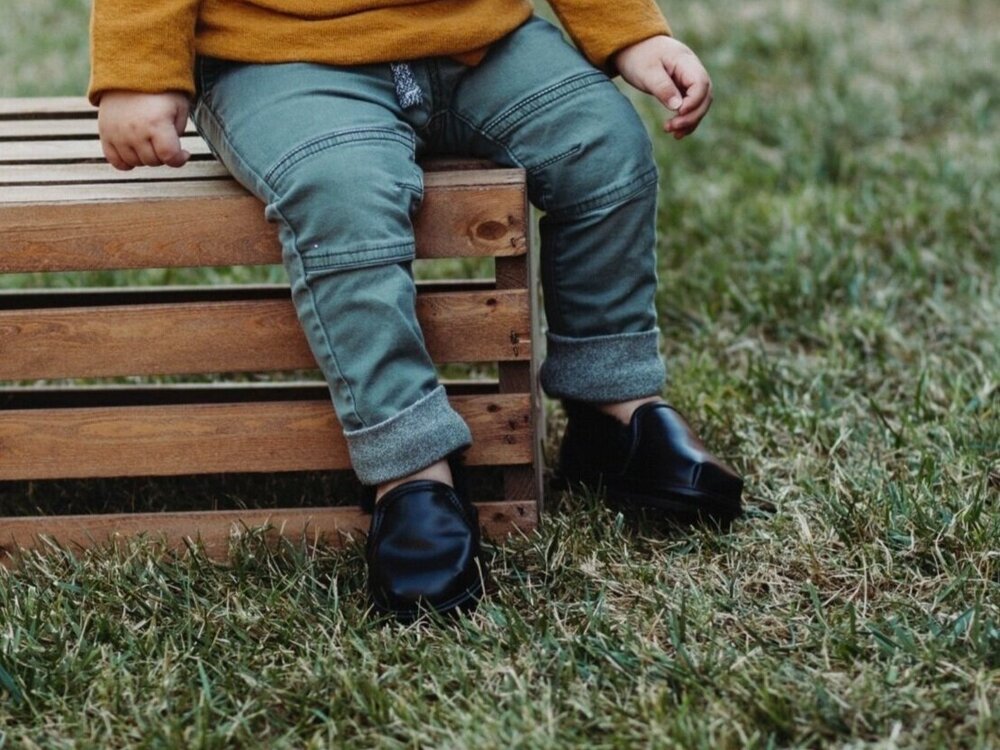Kids black slip-on shoes with wide toe box, two shoes shown on grass