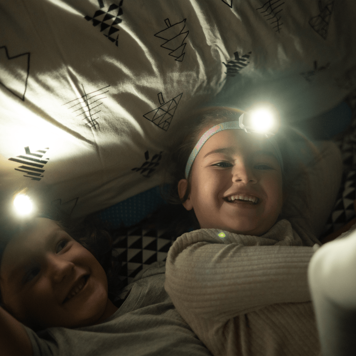 Kids headlamp glowing on child’s forehead under tent