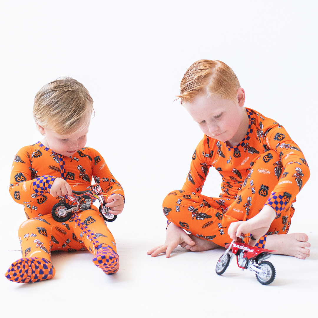 Orange pajama set on child knees; long-sleeve top and pants with racing print