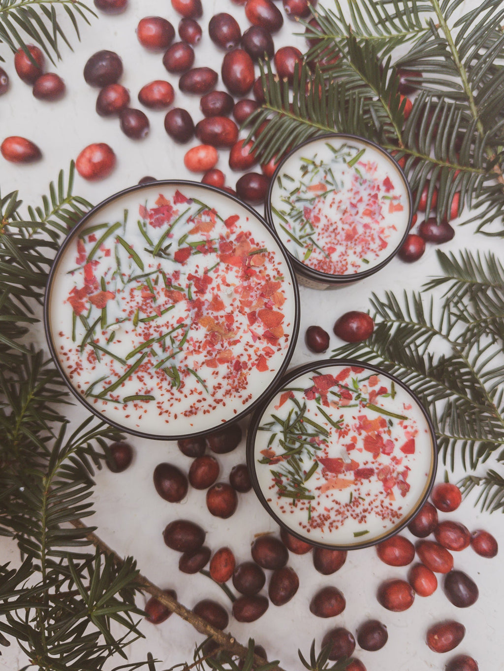 Three scented candle jars with pink wax and herb flecks, black lids and gold trim