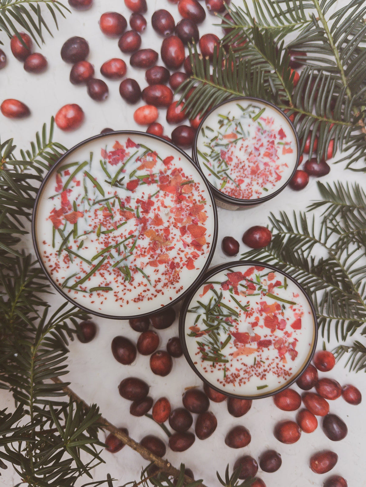 Three scented candle jars with pink wax and herb flecks, black lids and gold trim