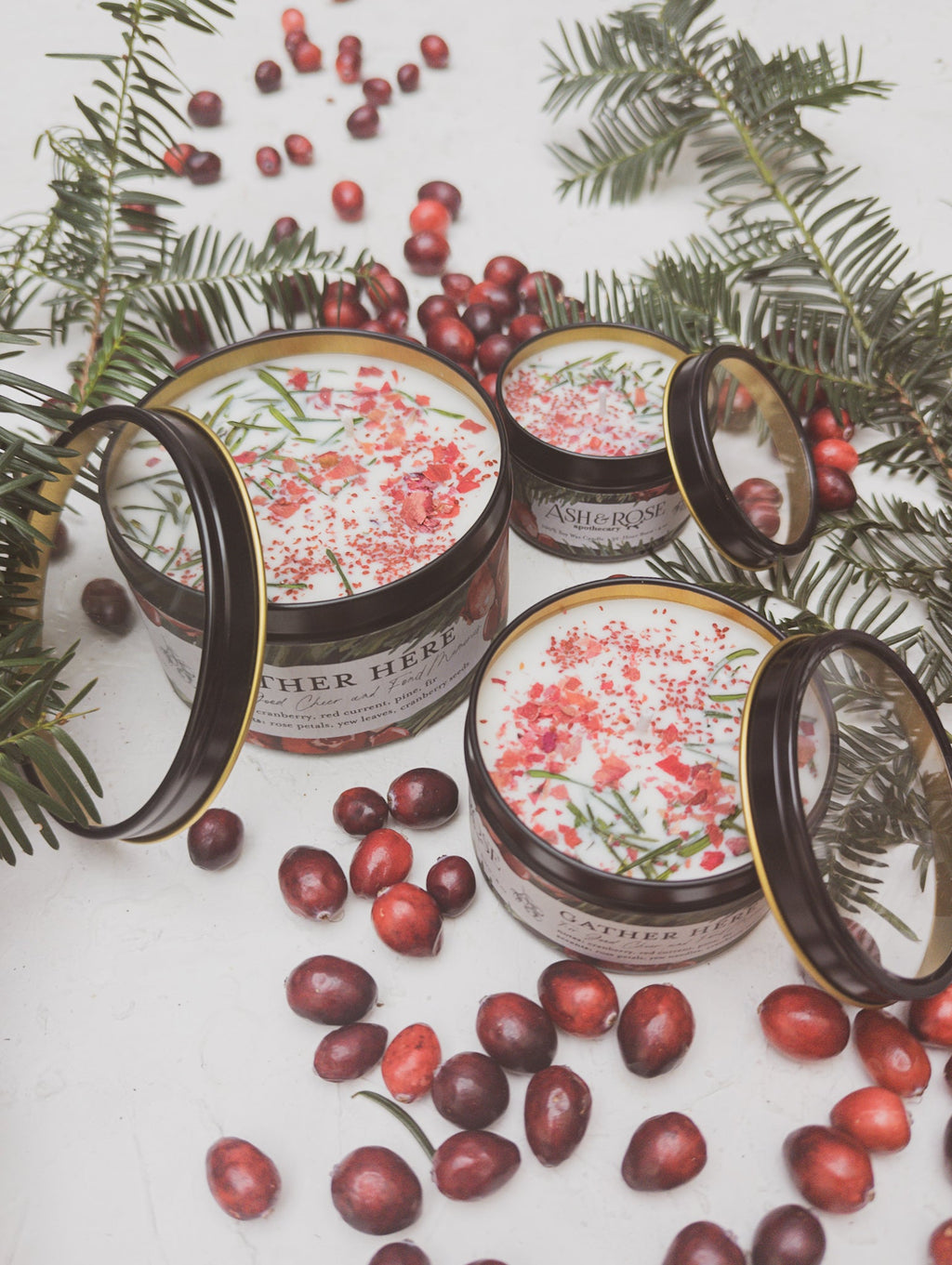 Scented candle jars with black lids and gold trim, pink wax with herb sprigs