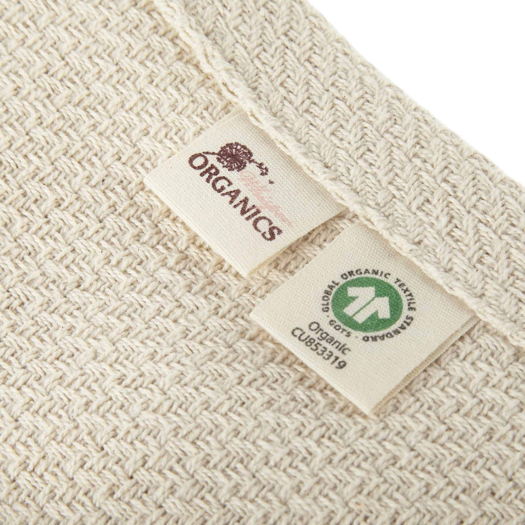 Natural woven blanket with stitched corner and visible organic fabric label.