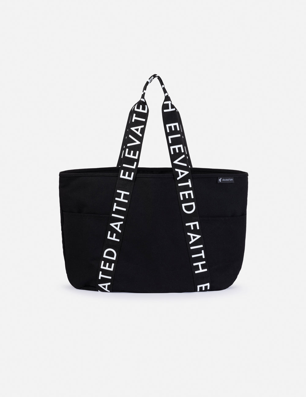 Black tote bag with long handles and vertical white 'ELEVATED FAITH' print.