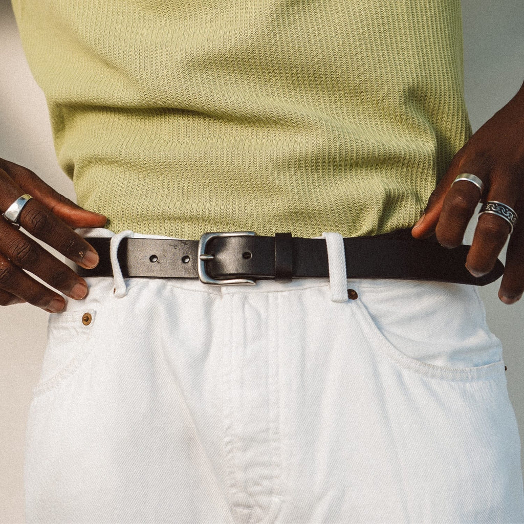 Leather stretch belt in dark style with metal buckle and eyelets, worn with white pants